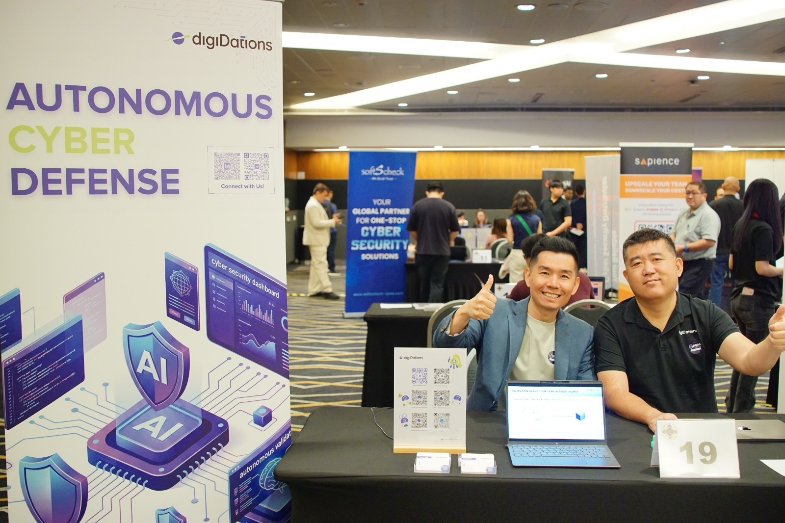 Two members of the digiDations team at Booth 19, beside an Autonomous Cyber Defense banner, at the DDAS Inaugural Talent and Solutions Showcase in Suntec Convention Centre.
